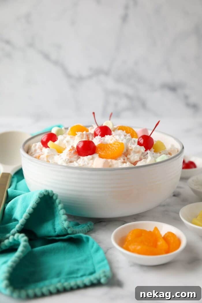 Side view of ambrosia salad in a bowl with canned mandarin oranges, pineapple tidbits, maraschino cherries, shredded coconut, mini marshmallows, Greek yogurt and Cool Whip.