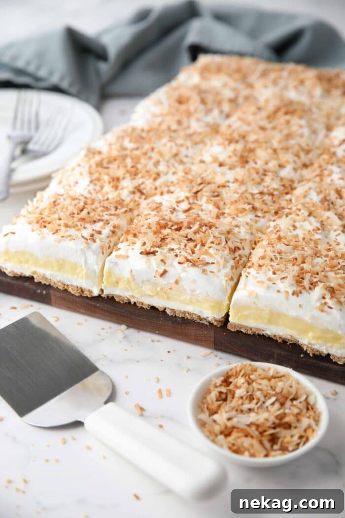 Coconut lush dessert with layers of graham cracker crust, cream cheese, coconut pudding, whipped topping, and toasted coconut.