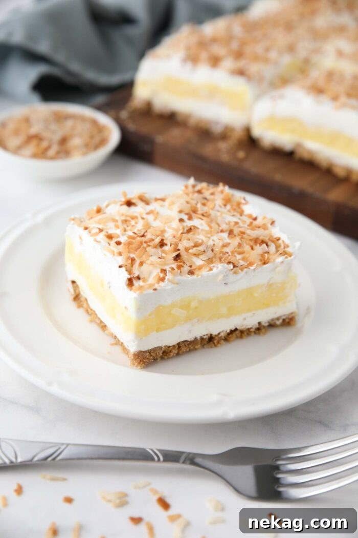 Coconut cream bars with layers of graham cracker crust, cream cheese, coconut pudding, whipped topping, and toasted coconut.
