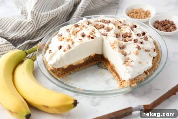 Slices removed from banoffee pie showing layers of graham cracker crust, dulce de leche caramel, bananas, whipped cream and toppings.