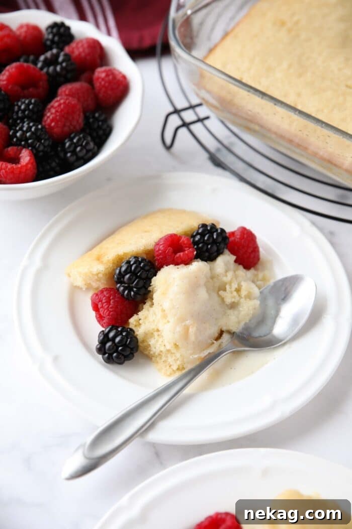 Scoop of homemade vanilla pudding cake on a plate with fresh berries.