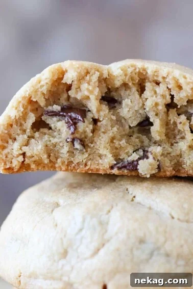 Two peanut butter chocolate chip cookies against a grey background with the top cookie sliced in half.