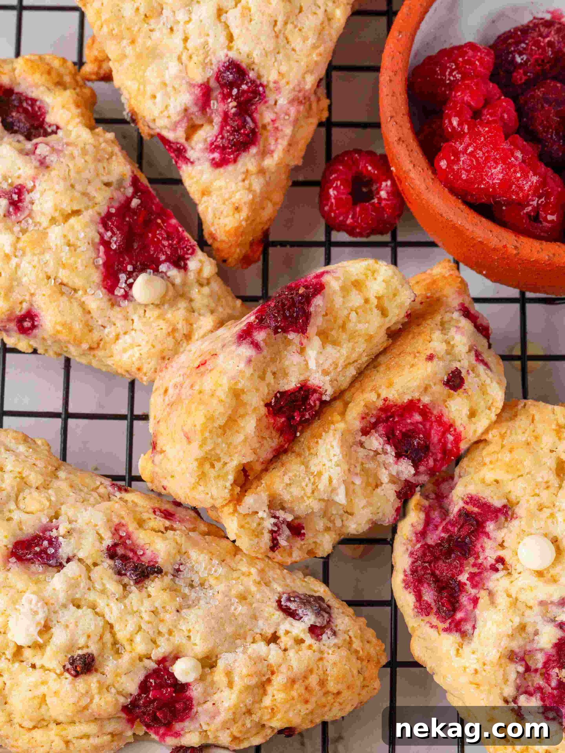 Raspberry white chocolate scones arranged on a wire rack with a small bowl of frozen raspberries beside.