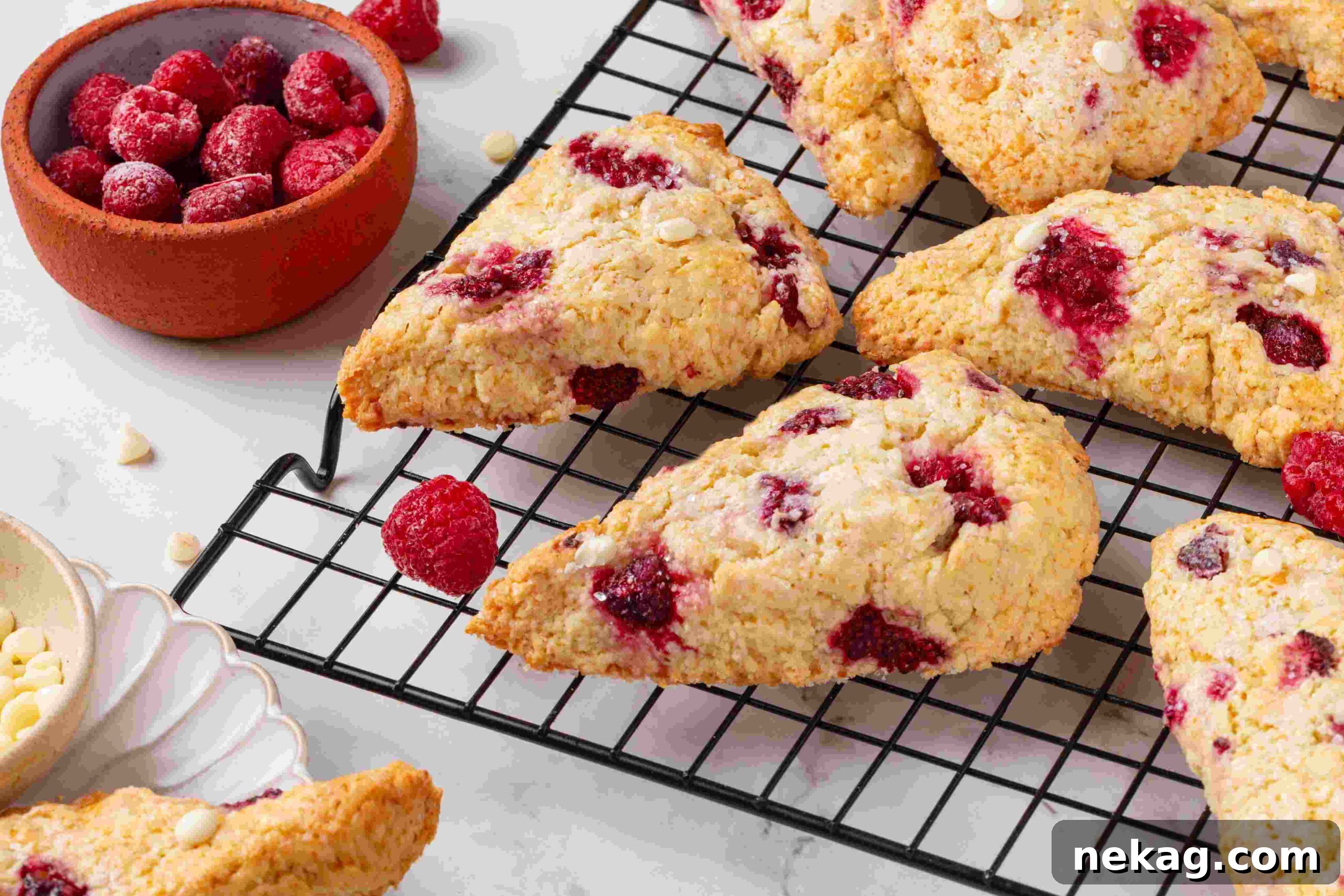 Raspberry white chocolate scones on a wire rack with a terracotta bowl of frozen raspberries beside.