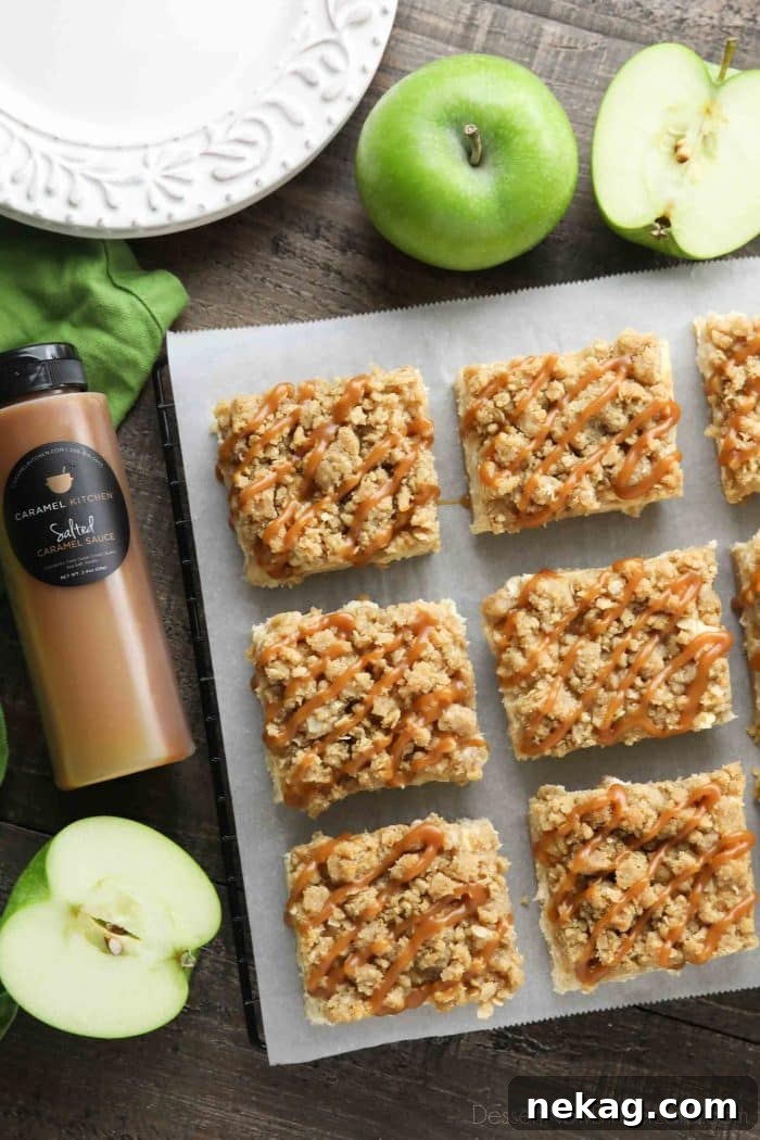 Squares of caramel apple cheesecake bars on parchment paper surrounded by Granny Smith apples and a bottle of salted caramel.
