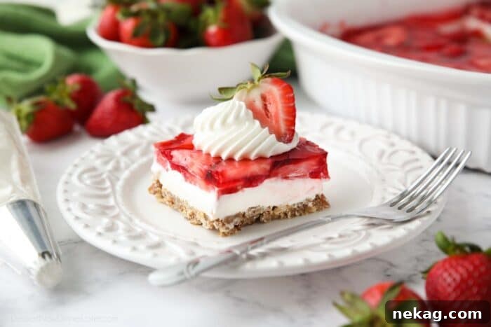 Piece of strawberry pretzel salad dessert on a plate topped with whipped cream and half of a strawberry.