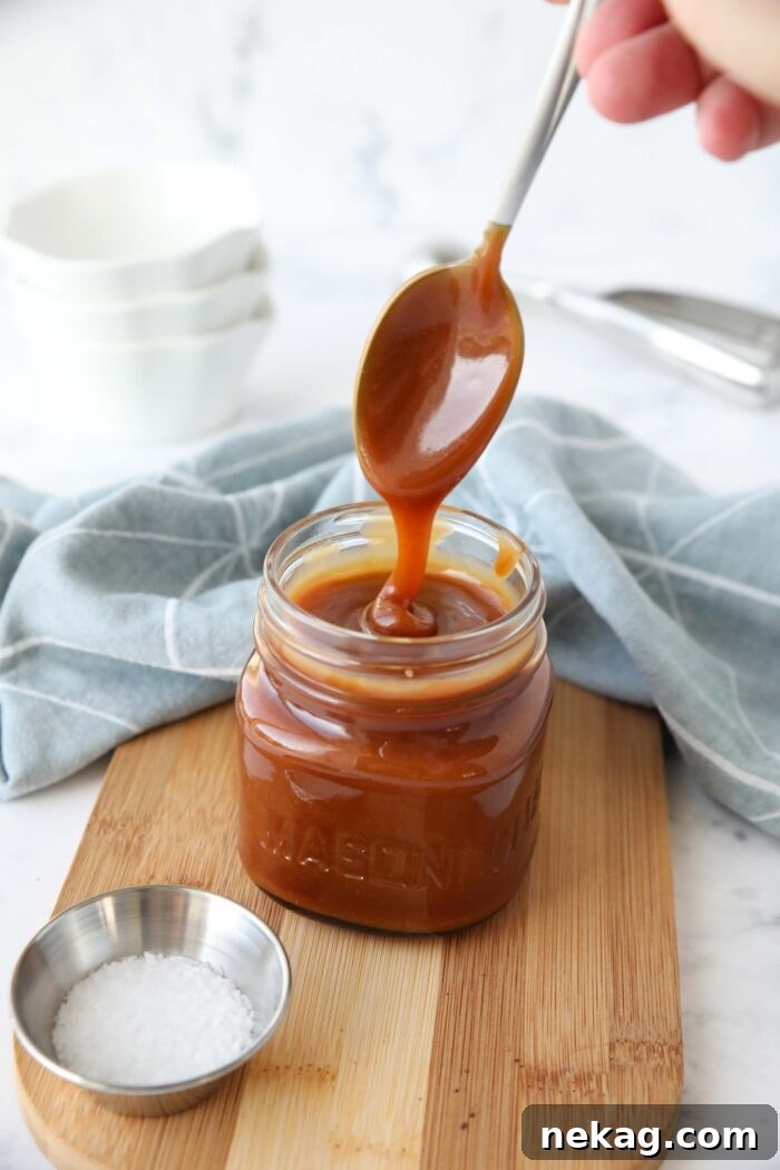 Homemade Salted Caramel Sauce Recipe 2 Homemade salted caramel sauce in a jar being drizzled with a spoon.